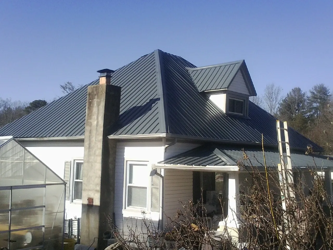 Dark blue standing seam metal roof on a white farmhouse with dormer — Slate & Tile Roof Repair by Roofing Brothers in Mantador