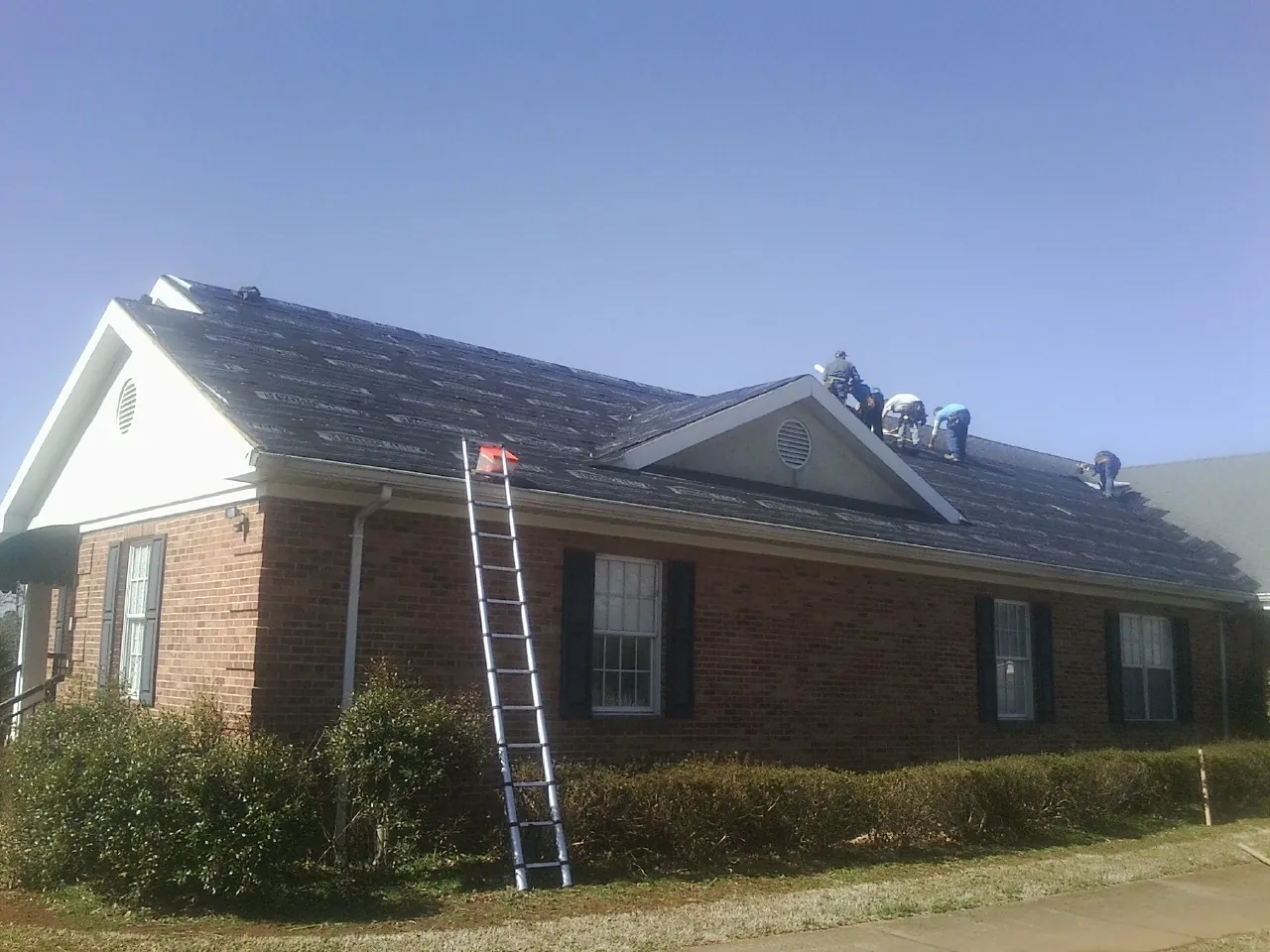 Crew tearing shingles off a brick ranch roof with a ladder set — Emergency Roof Repair work by our crew in Mantador