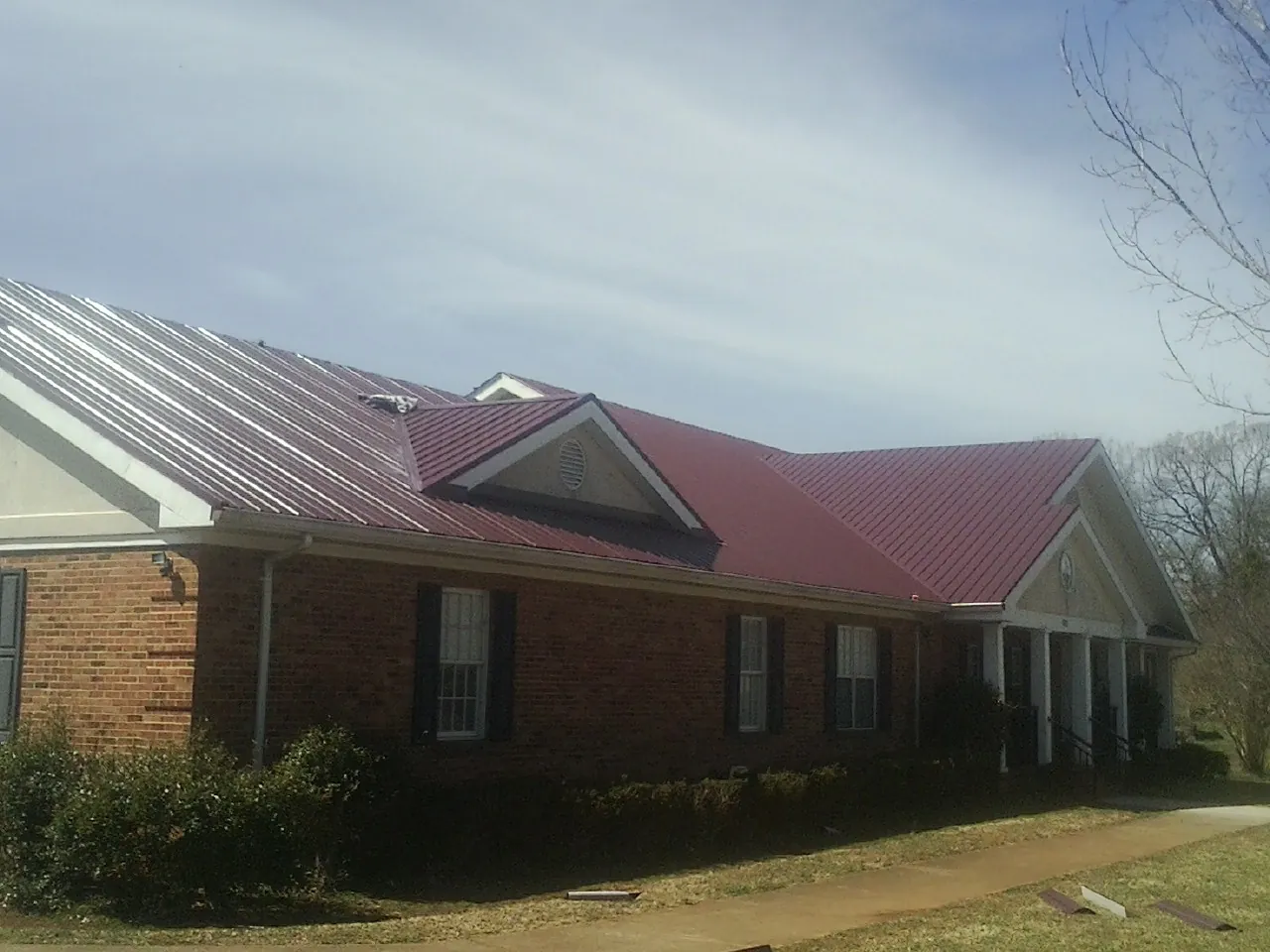 Red metal roof with gabled entries on a long brick building, from a Hail Damage Roof Repair job in Mantador