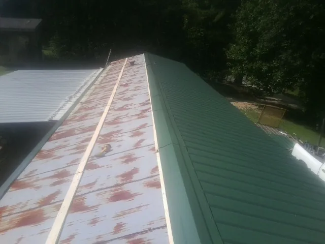 Old rusted panels beside newly installed green metal roofing — Wind Damage Roof Repair by Roofing Brothers in Mantador