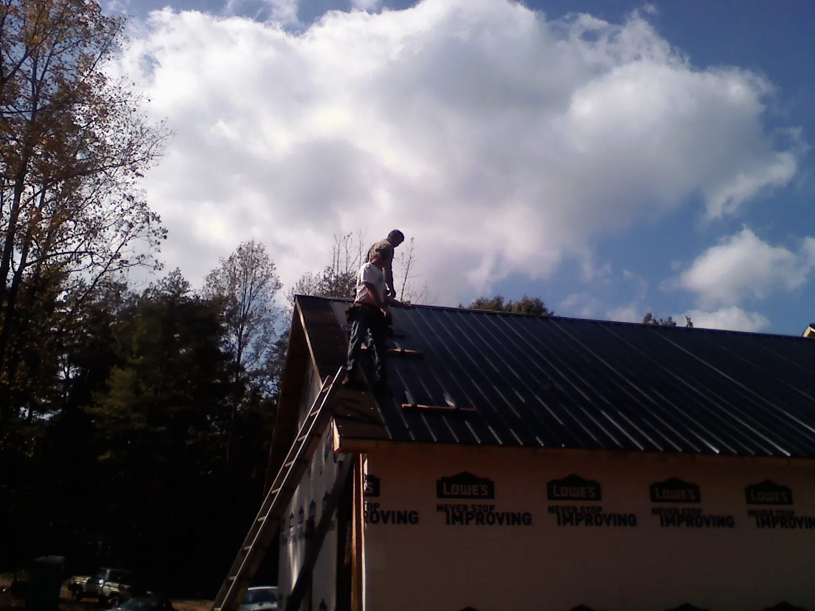 Roofer fastening dark metal panels high against a cloudy sky, from a Roof Inspection job in Mantador