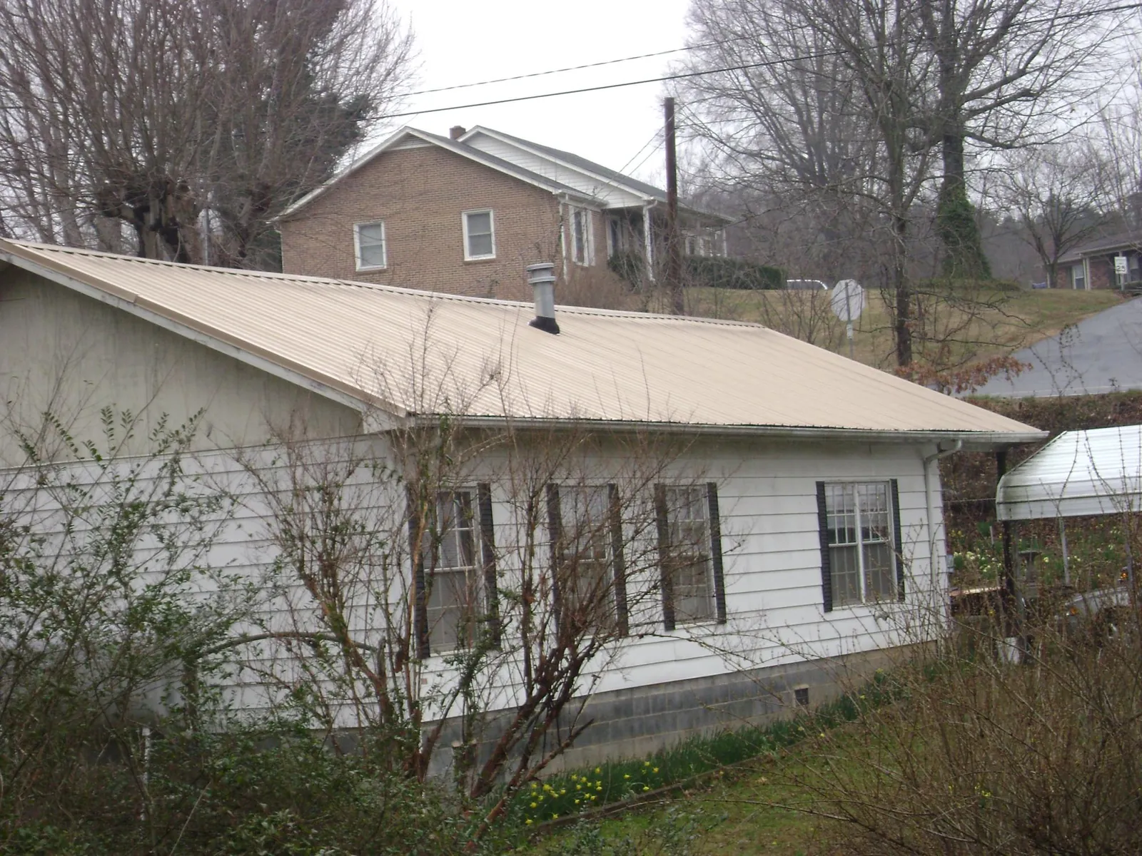 Tan metal roof on a white sided house set into a hillside — Commercial Roofing by Roofing Brothers in Mantador