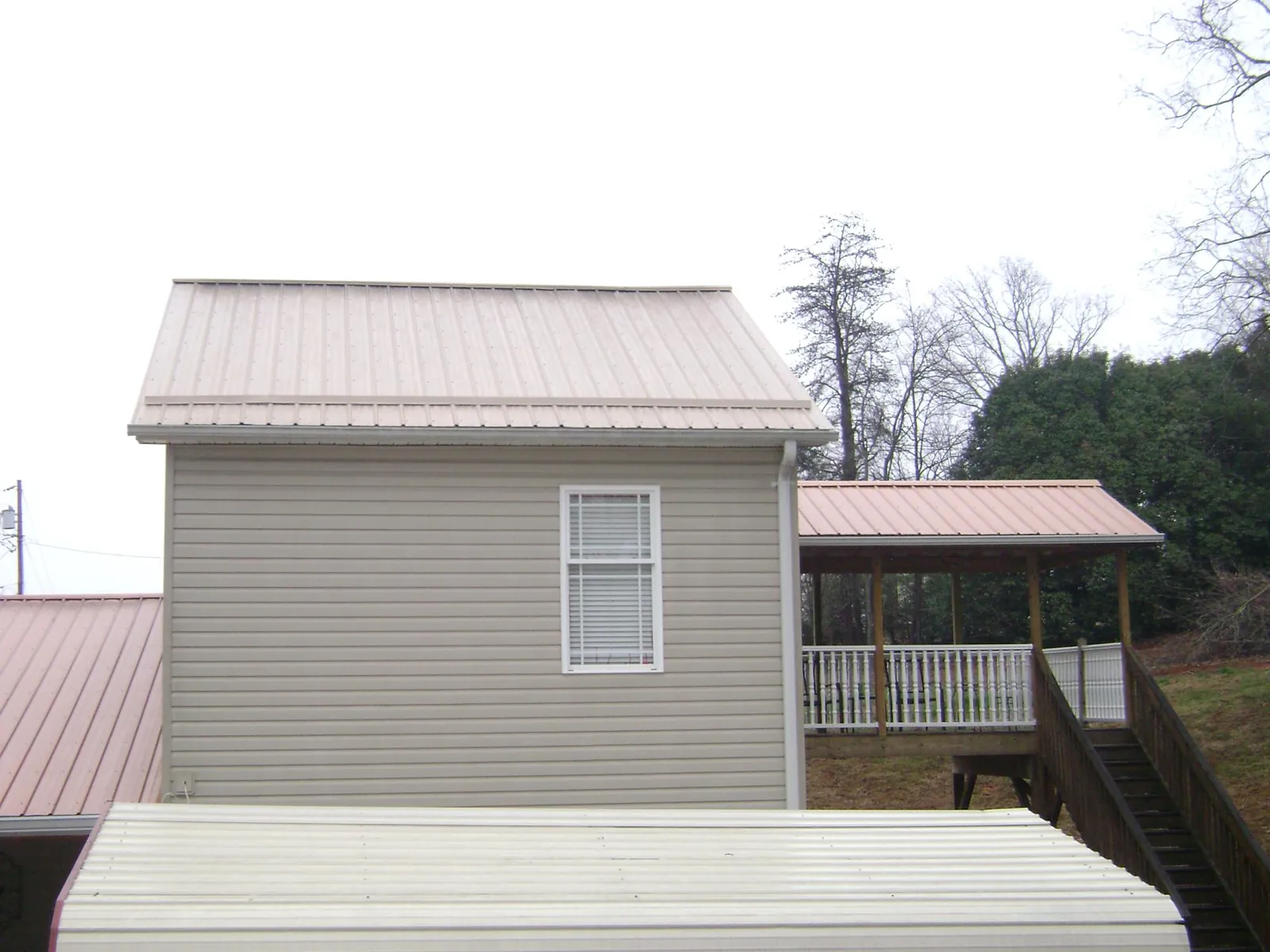 Tan metal roofs on a two story addition and attached porch, from a Roof Replacement job in Mantador